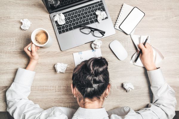 Frau hat Kopf auf Schreibtisch gelegt, um ihren Laptop herum ist Chaos