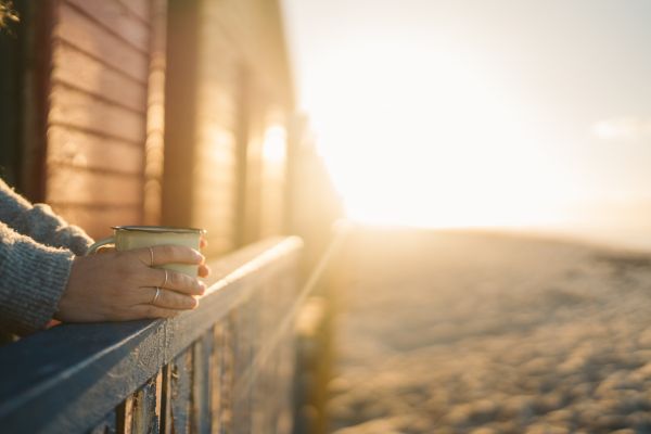 Sonnenaufgang am Strand, sichtbar sind Hände auf einer Terrasse, die eine Tasse halten